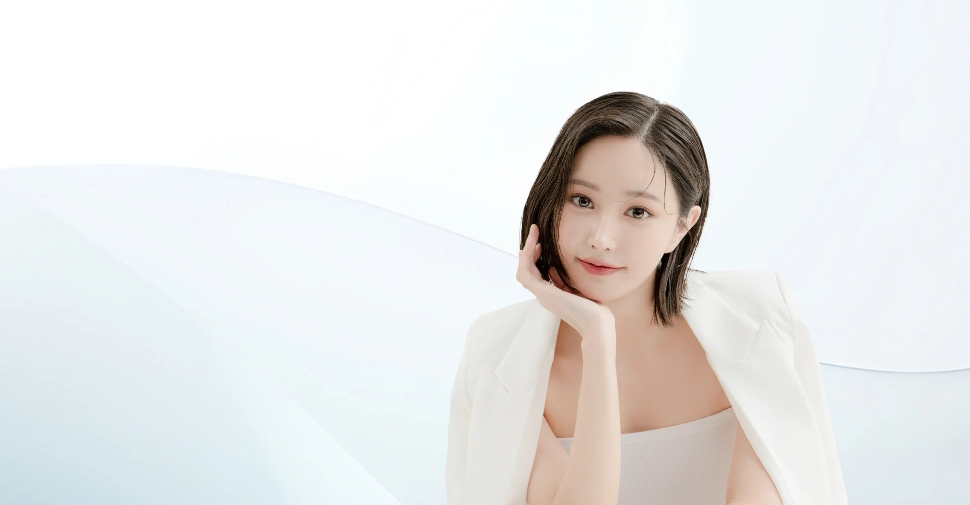 白いジャケットを着た女性が顎に手を当てて微笑んでいる。